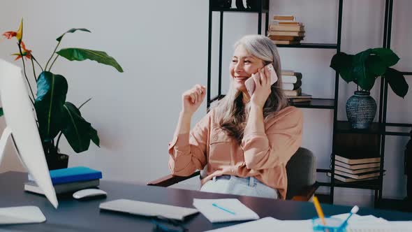 Attractive Successful Elderly Businesswoman Making Phone Call in Modern Office Sitting at Desk with