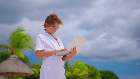 A Student is Engaged in Selfeducation Sitting on the Beach Against the Background of the Turquoise