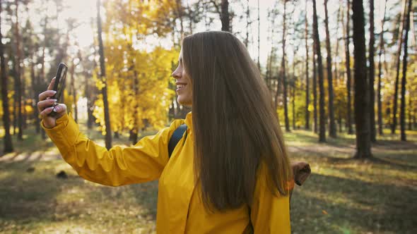 Young Lady Smiling Taking Pictures of Environment on Her Mobile Phone During Walk in Autumn Wood