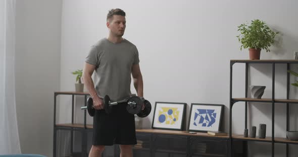 Young Sporty Man Is Training with Dumbbells Tensing Muscles of Arms and Upper Body Lifting Weights