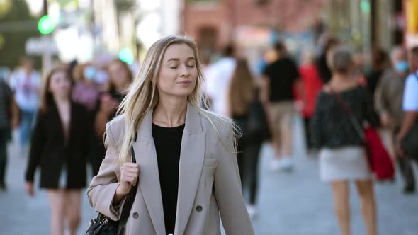 Lovely blonde girl walking on city streets background. Attractive smiling lady.