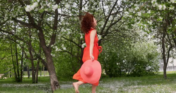 Woman in a Red Dress Runs Through the Park with Flowering Trees