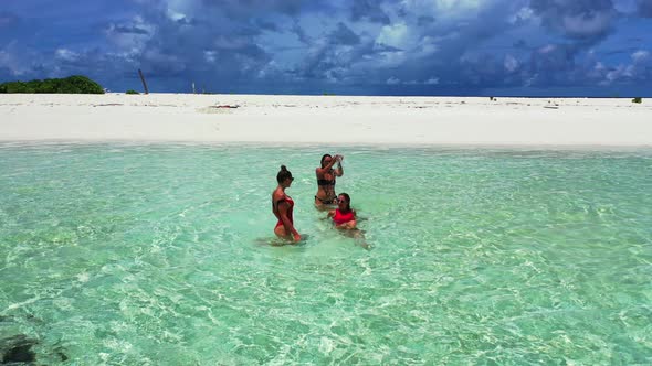 Pretty fun women on photoshoot enjoying life on the beach on clean white sand and blue 4K background