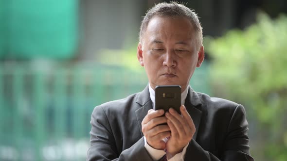 Mature Japanese Businessman Using Phone in the Streets Outdoors