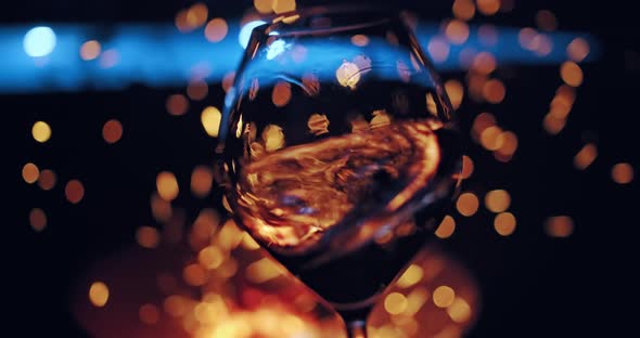 Closeup of Female Hand Waving Wine in a Glass on Defocused Cozy Camp Fire of Background