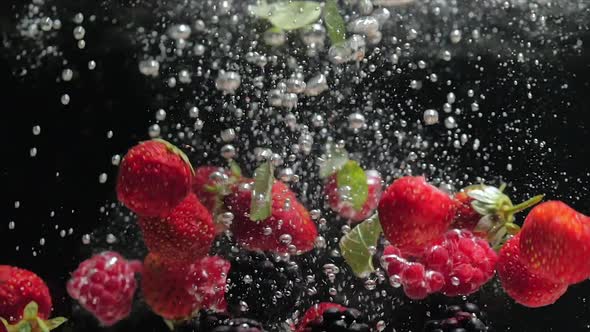 Fresh Raspberries with Blueberries and Fresh Mint Leaves Fall on a Black Background Into the Water