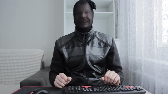 A Hacker and Internet Scammer in a Black Stocking on His Head Smiles at the Camera in Front of a