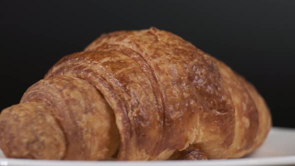 Croissant on white plate rotating in front of camera on black background