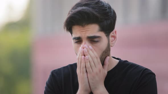 Stressed Bearded Indian Allergic Young Man Sneezing with Hands in Front of Face Outdoors