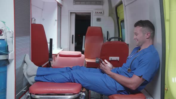 Man Sit with Phone in Ambulance Car, Watch Something and Smile.