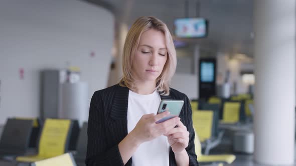 An Attractive Young Woman at the Airport is Texting with Friends on Her Smartphone