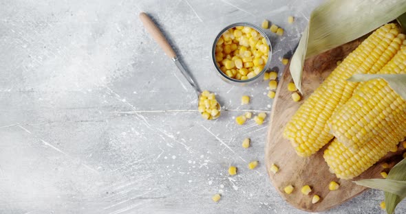 Canned Corn in a Tin and Fresh Corn with Leaves on a Cutting Board.