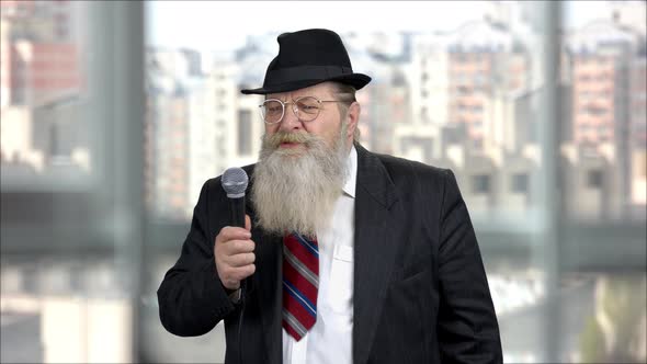 Senior Longbearded Man Giving Speech with Microphone Indoor