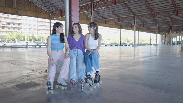 Three Girls Wearing Roller Skates Sit and Talk and Laugh Handheld