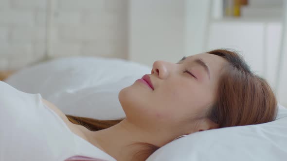 Close up on face Asian young woman close her eyes lying on bed and sleep in cozy bedroom