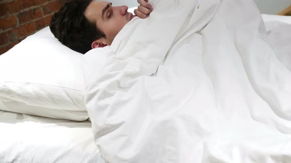 Young Man peeking out from Blanket in bed