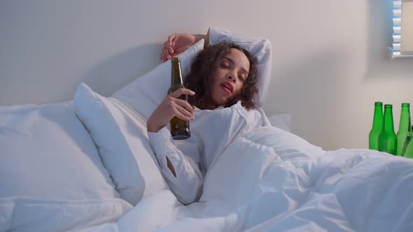 Drunk Latino woman hold beer bottle, feel hangover and dancing on bed.