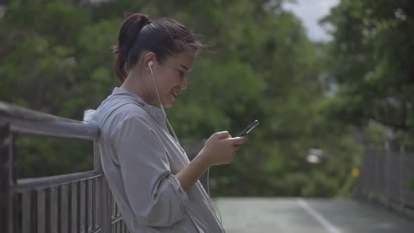 Smiling portrait beautiful young Asian woman fitness runner standing using mobile phone.