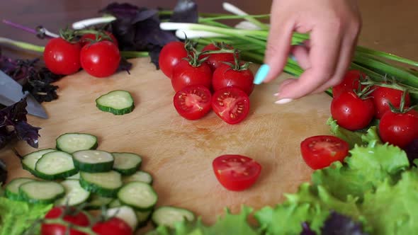 Closeup Woman Cuts Cherry Tomatoes on a Wooden Cutting Board