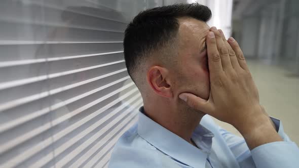 Closeup Side View of Desperate Businessman Sitting in Office Hallway Holding Head in Hands