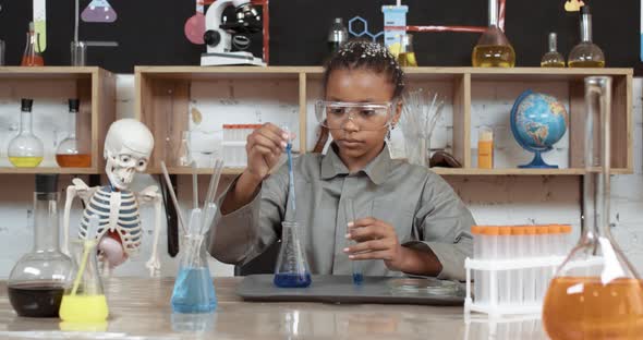 Laboratory Experience in a Chemistry Lesson, African Girl in Protective Glasses Pours a Blue Liquid