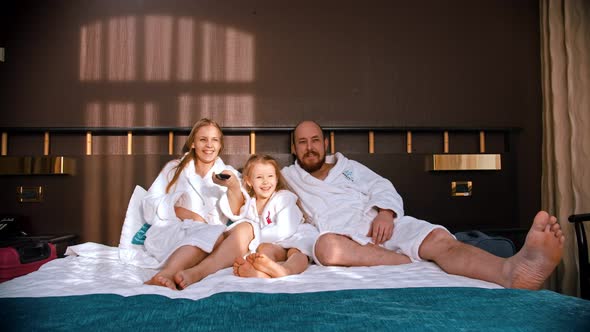 A Family in White Bathrobes Sitting in the Bed and Watching TV