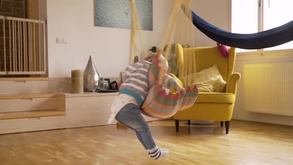 Adorable infant boy rotating in cushioned single swing at living room.
