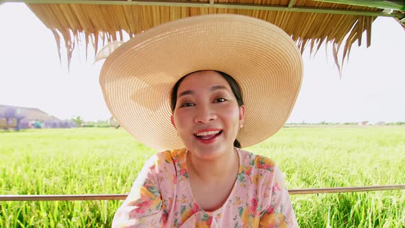 Beautiful young Asian woman with hat in rice field making video call.