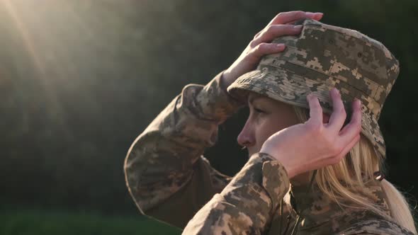 Female Soldier Puts on Camouflage Hat on Head Outdoors