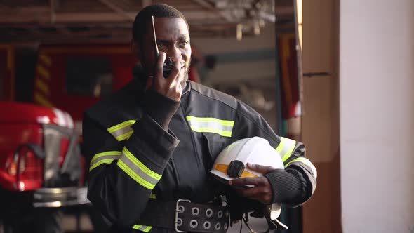 African American Fireman in Equipment with Helmet Use Walkie Talkie at the Station