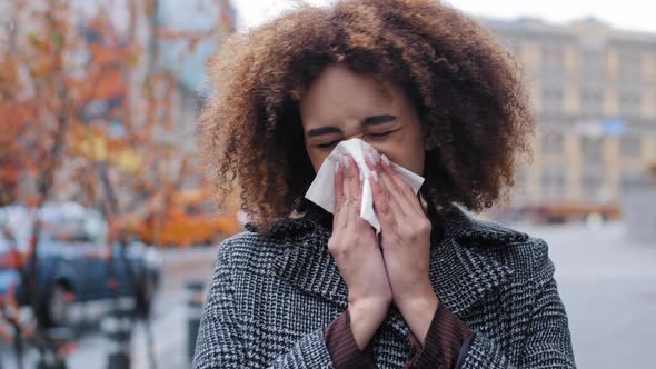 Sick Ill African American Woman with Curly Hair Blowing Runny Nose Into Tissue Paper Outdoors Cold