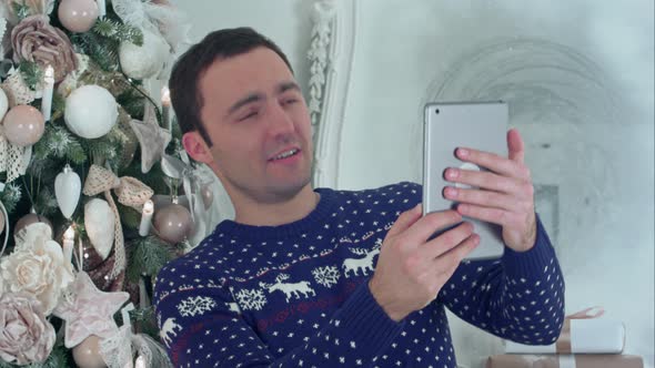 Young Handsome Man in a Christmas Knitted Sweater Taking Selfies on a Tablet