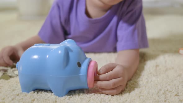 kid boy preschool putting pin money coins into blue faced piglet slot