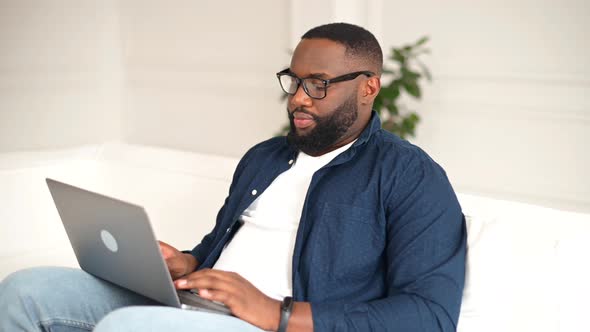 Side View at Young Modern AfricanAmerican Freelancer Guy Using Laptop