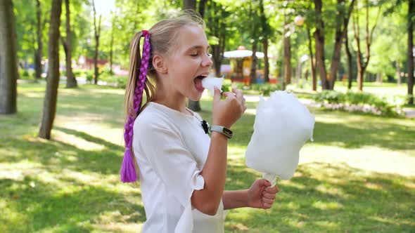 Joyful Teenager Girl in the Park Eats Cotton Candy. alt