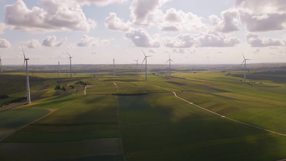 Soft clouds floating by over a wind park in rural Germany. Aerial wide angle pull back shot