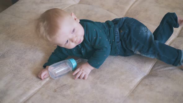 Cute Child Plays with Bottle Crawling on Bed at Home