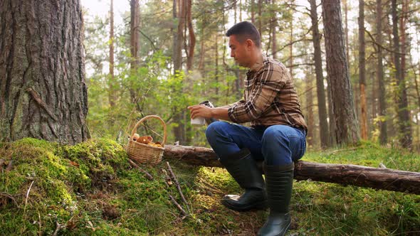 Man with Basket of Mushrooms Drinks Tea in Forest