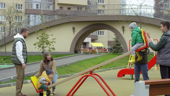 Two Friendly Couples Entertaining their Kids on Seesaw