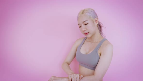 Asian young woman doing her arm massage in front of pink background