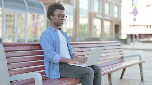 Young African Man with Laptop Smiling at Camera While Sitting Outdoor on Bench