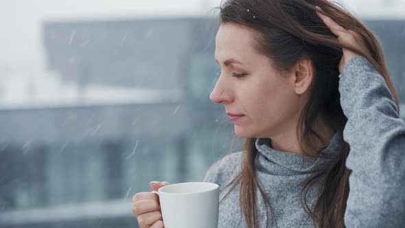 Woman Stays on Balcony During Snowfall with Cup of Hot Coffee or Tea