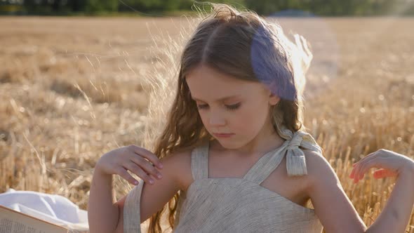 Serious Child Girl with Long Hair Sits on a Mown Wheat Field