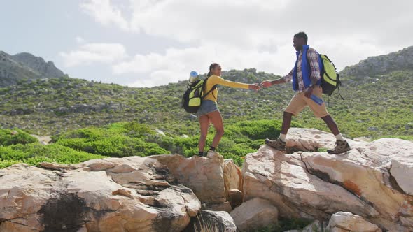 African american couple holding each others hands and walking on the rocks while hiking