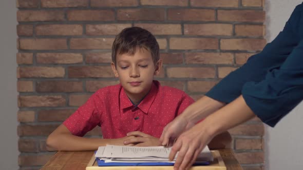 Child Sitting at the Desk Holding Flipchart with Lettering Staff on the Background Red Brick Wall.