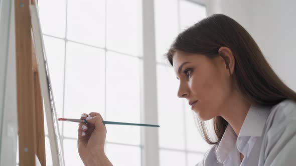 Woman Draws Red Flowers on Canvas Sitting Near Large Window