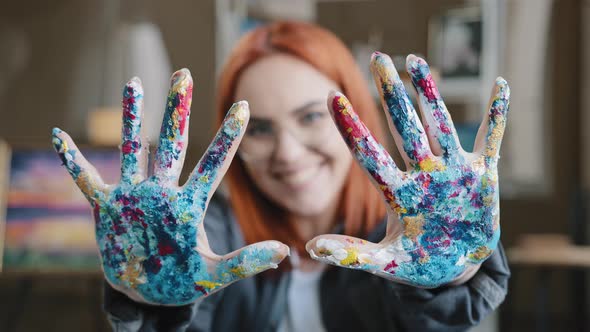 Closeup Happy Funy Woman with Red Hair Painter Girl Artist in Glasses Looks at Camera Stretches