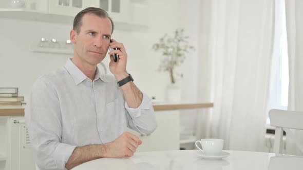 Cheerful Middle Aged Man Talking on Smartphone at Home