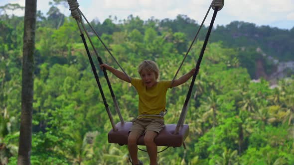 Slowmotion Shot of a Little Boy Swinging on Swings in a Tropical Surrounding. Travel To Bali Concept